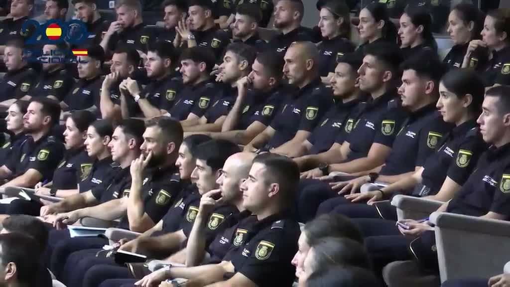 Alumnos y agentes de la Policía Nacional sentados uniformados en un anfiteatro durante una sesión informativa previa al despliegue.
