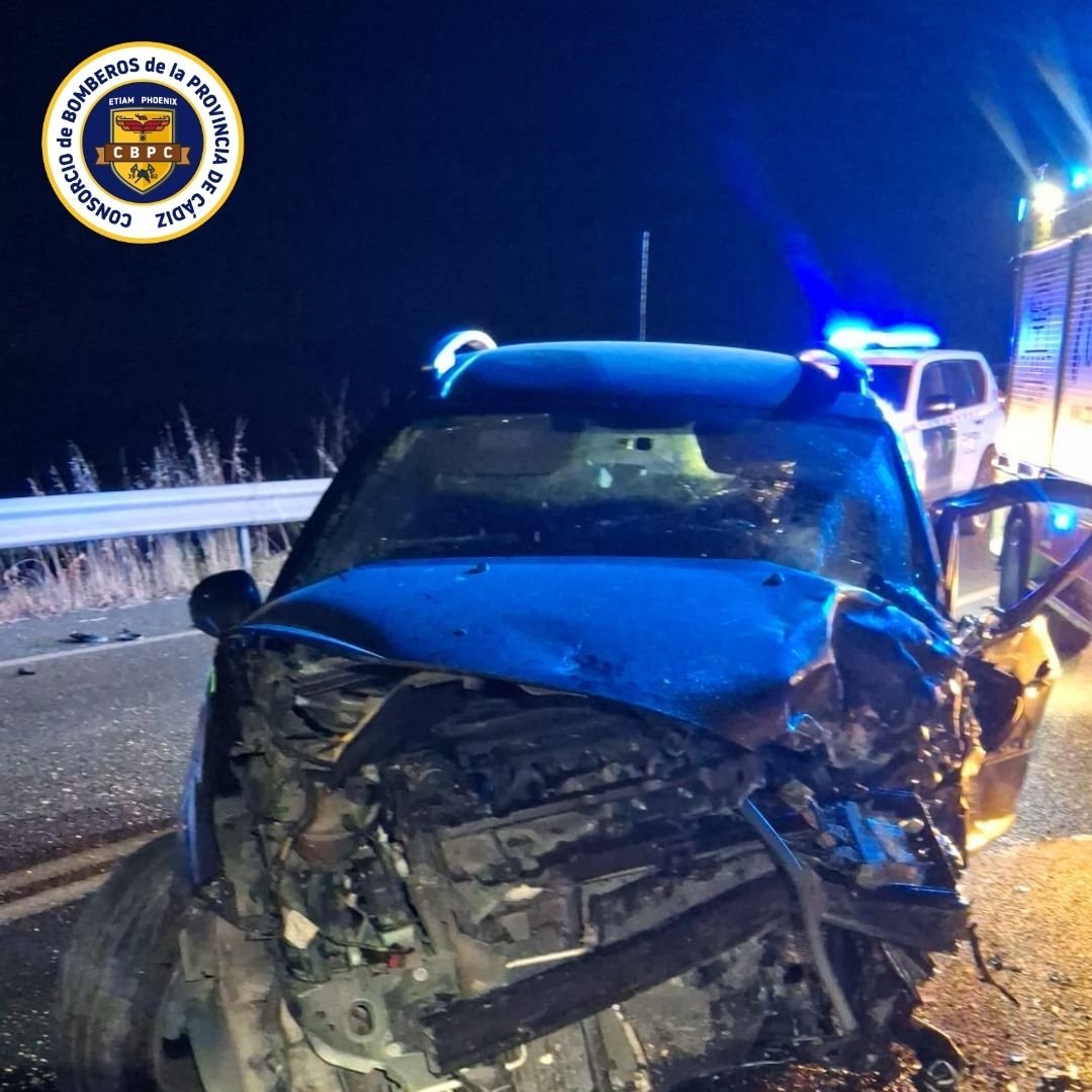 Coche con el capó y la parte frontal completamente destrozados por un choque nocturno en la carretera A-471, con un vehículo policial y luces de emergencia de fondo.