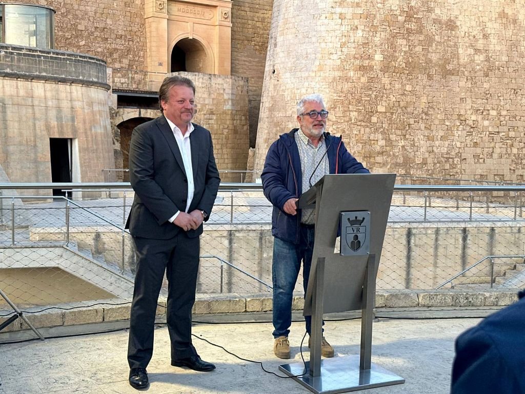 El coordinador Patricio Pérez Pacheco pronuncia su discurso bilingüe en el atril de la Citadella de Gozo al lado del alcalde Brian Azzopardi.