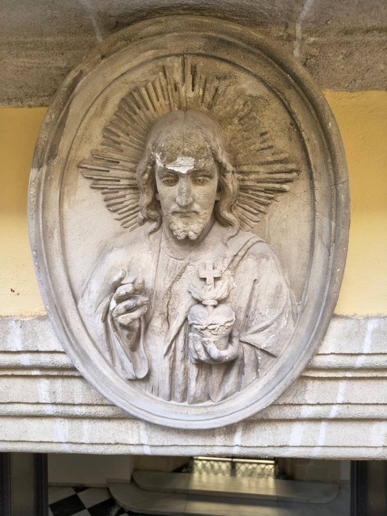 Medallón de piedra ovalado con el altorrelieve del Sagrado Corazón de Jesús esculpido sobre la puerta del Ayuntamiento de Jerez.