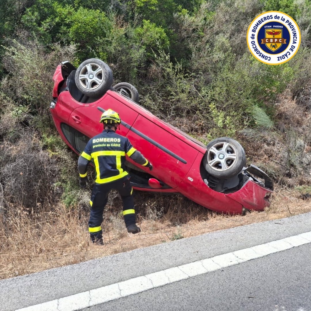 Bombero del Consorcio de la Provincia de Cádiz inspeccionando un vehículo rojo volcado tras un accidente de tráfico en la carretera A-373 en Ubrique.