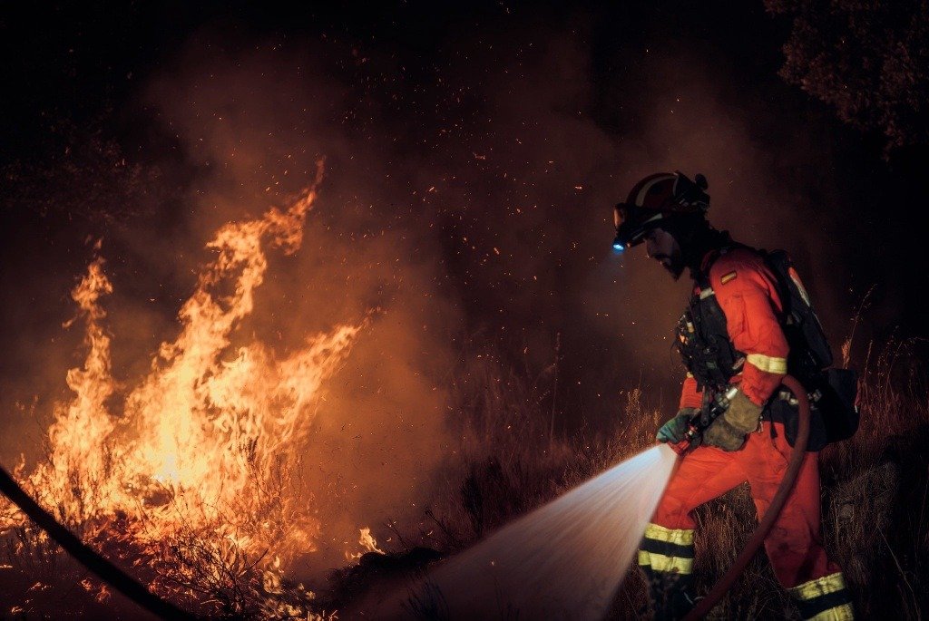 Bombero forestal equipado con uniforme técnico y linterna frontal trabajando en la extinción de un frente de fuego nocturno.