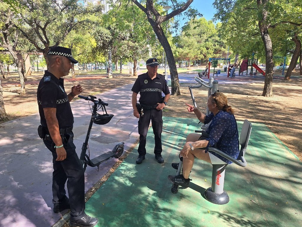 Agentes de la Policía Local informando a una ciudadana sobre la normativa de uso de patinetes eléctricos en una zona de parque.