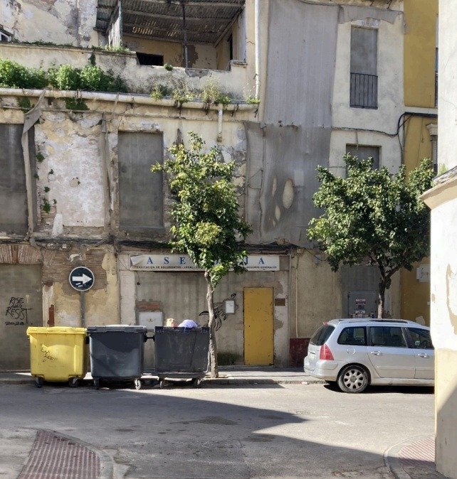 Fachada de edificio deteriorado en el centro de Jerez, con contenedores de basura y un vehículo estacionado en primer plano.