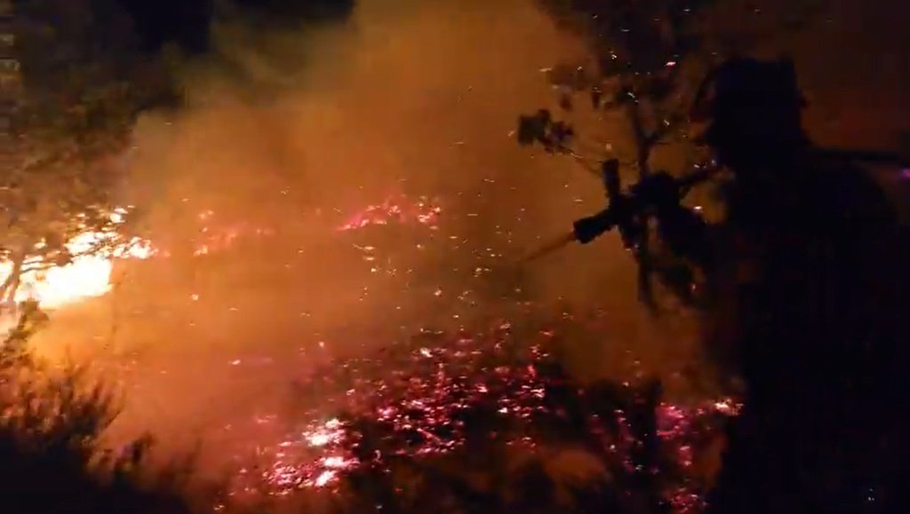 Efectivo de emergencias trabajando en la extinción de un frente de fuego nocturno, rodeado por llamas y densa humareda.