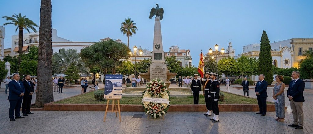 Homenaje oficial en la Plaza de las Angustias por el centenario de Juan Manuel Durán en Jerez, mostrando el monumento del águila con una corona de flores, autoridades locales y miembros de la Armada Española en formación.