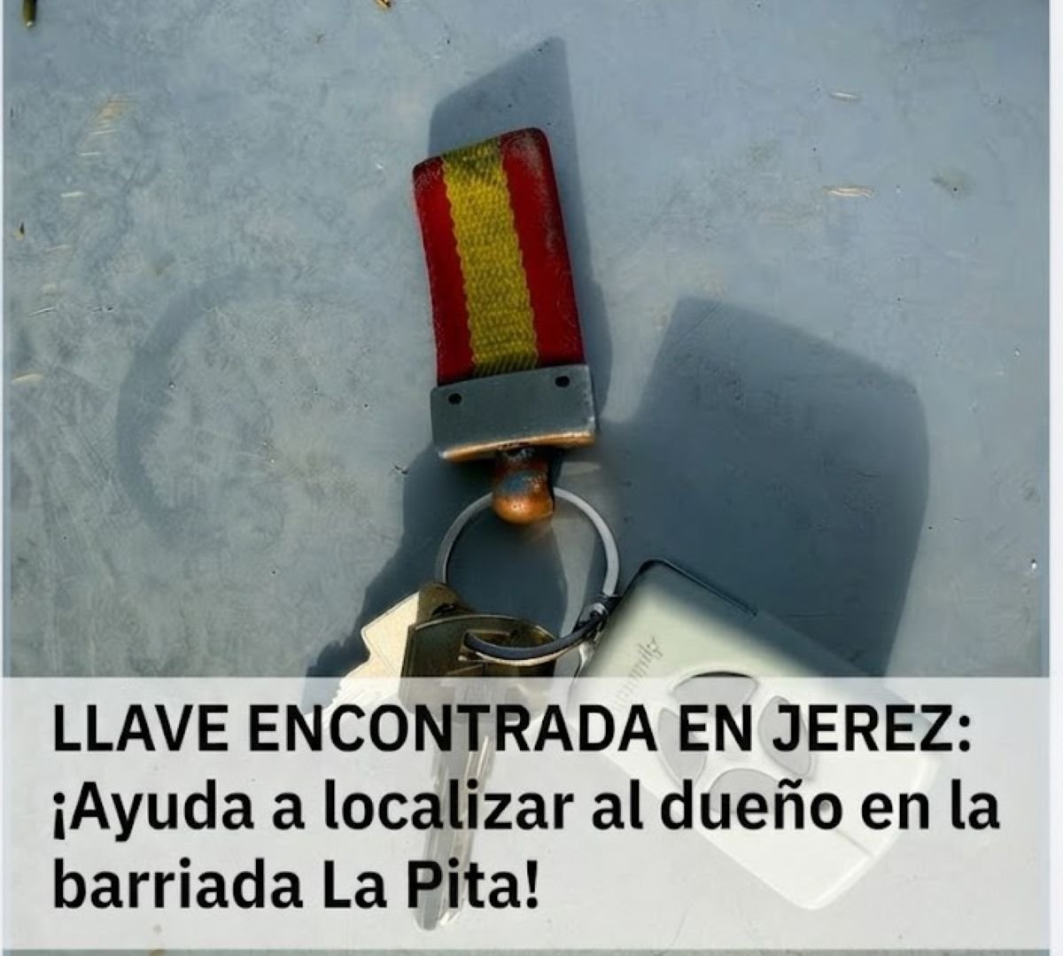 Llavero con cinta de los colores de la bandera de España que incluye una llave metálica y un mando de garaje gris sobre una superficie clara.