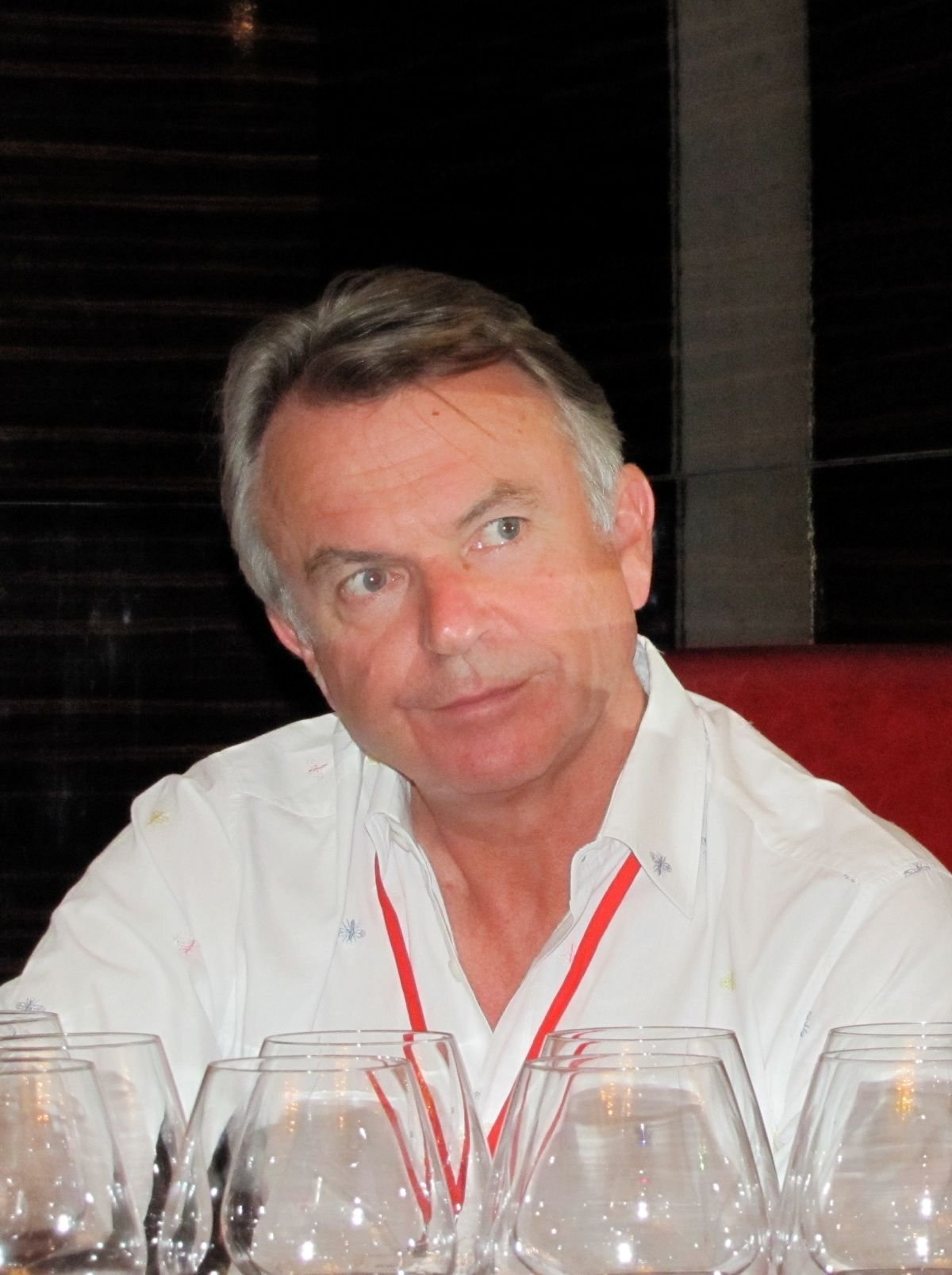 Primer plano de Sam Neill asistiendo a un evento de cata de vinos, mostrando su faceta personal vinculada a la viticultura.