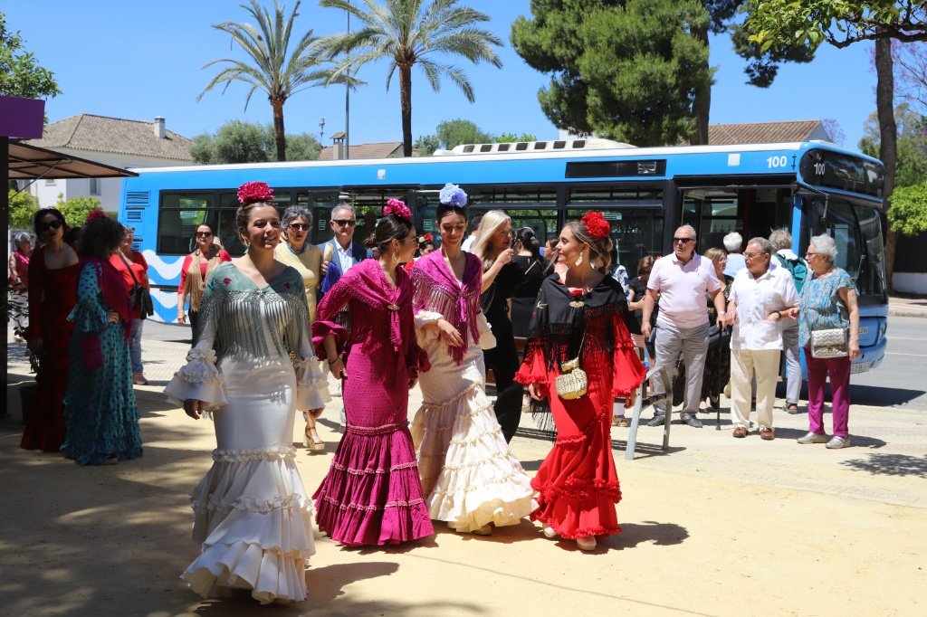 Ciudadanas vestidas con trajes de flamenca descendiendo de un autobús urbano moderno durante la Feria del Caballo en Jerez.