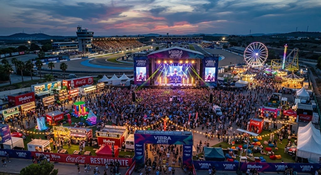 Vista aérea del recinto del festival Vibra Jerez con el escenario principal iluminado, zona de comida y noria al atardecer.