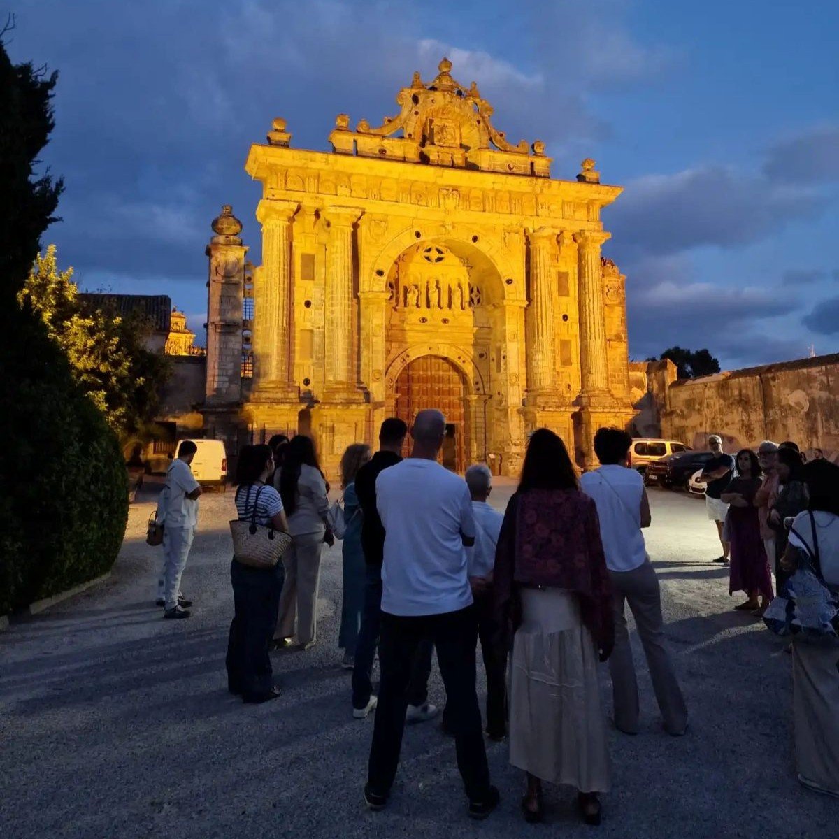 Grupo de visitantes contemplando la fachada iluminada del Monasterio de la Cartuja de Jerez durante una visita nocturna.