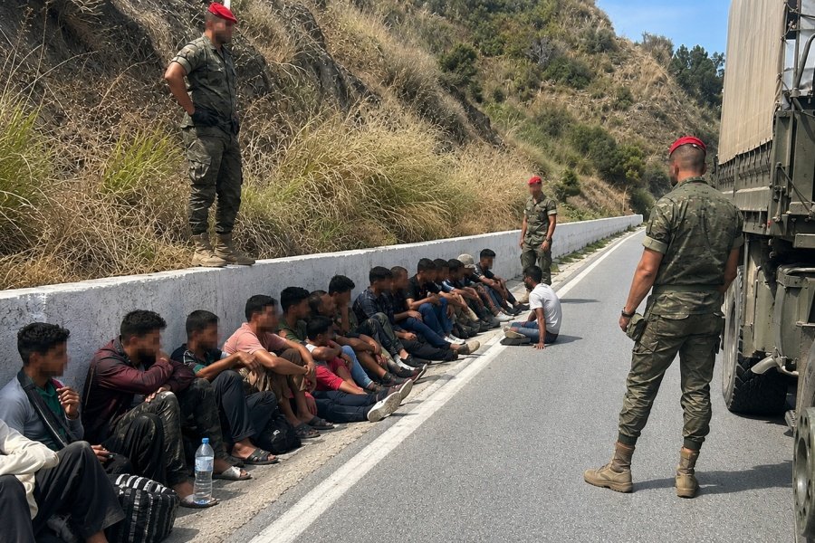 Militares del Ejercito de Tierra vigilando a un grupo de migrantes sentados en la cuneta de una carretera en Ceuta