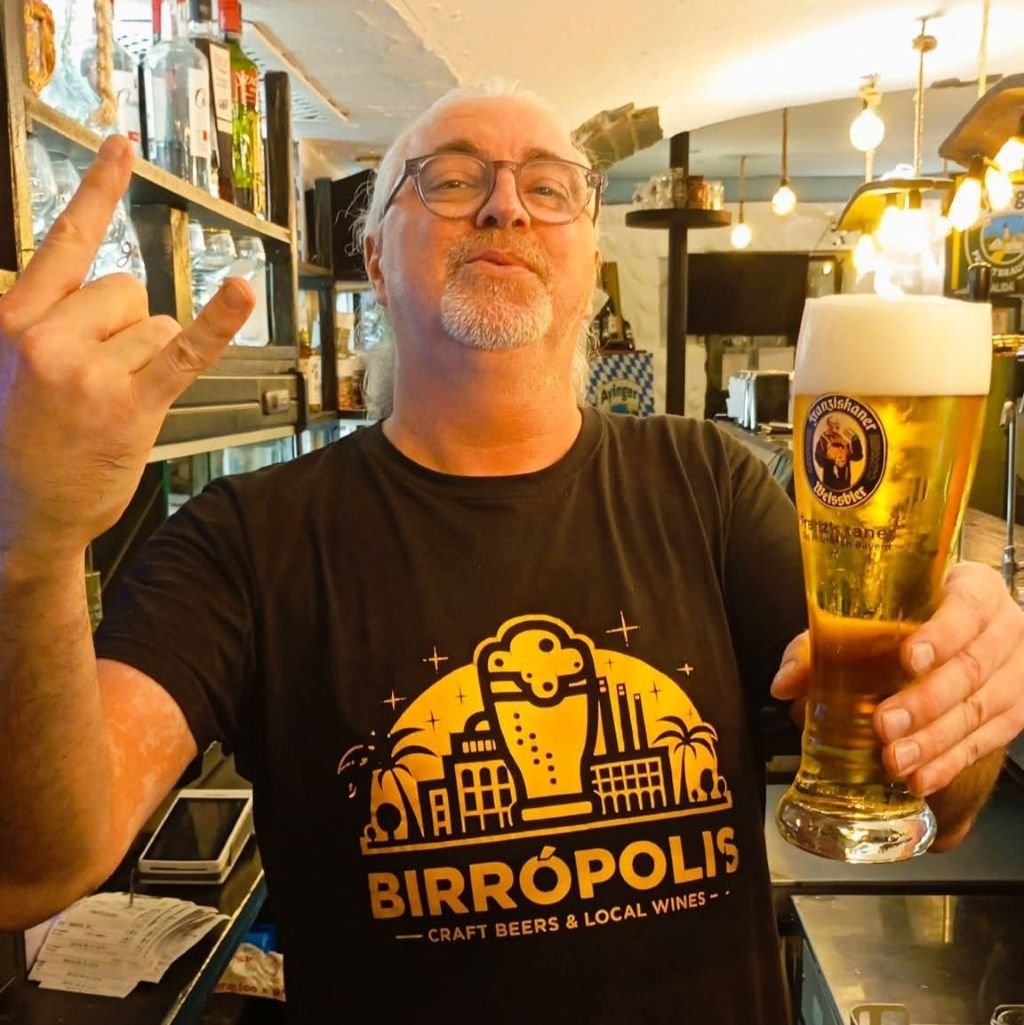 Jimmy, el encargado de Birrópolis en Jerez, posa tras la barra con una camiseta del local y un vaso de cerveza artesana haciendo el gesto de rock.