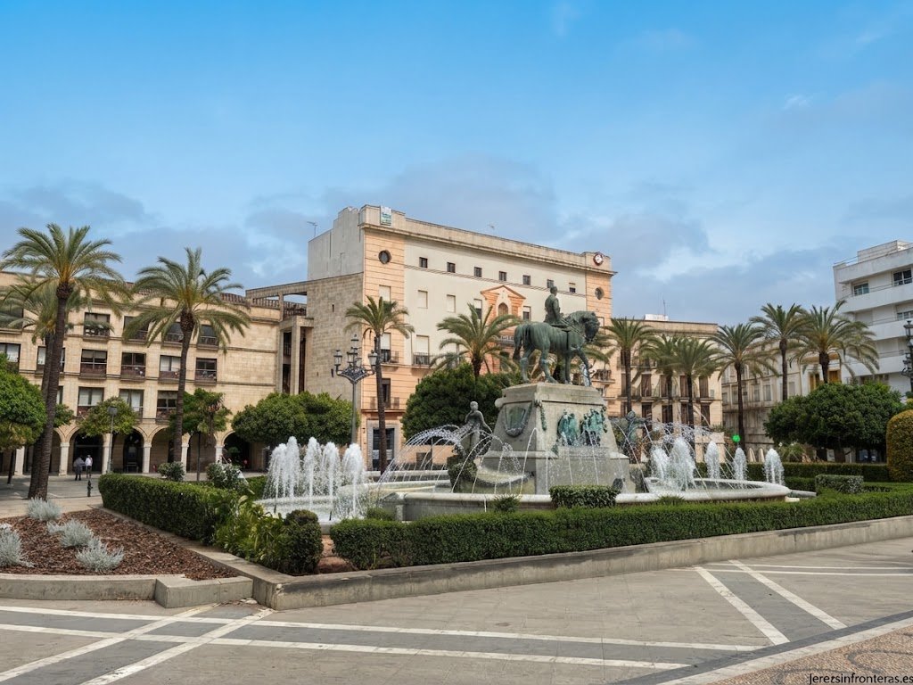Fotografía a nivel de suelo de la fuente ornamental y la estatua ecuestre de Primo de Rivera en la Plaza del Arenal de Jerez de la Frontera, con el cielo nublado de fondo.