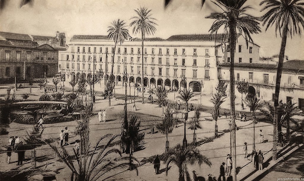 Fotografía histórica en blanco y negro restaurada digitalmente y mejorada en su calidad y resolución de la Plaza del Arenal de Jerez, mostrando los soportales y la clásica arboleda de palmeras con mayor nitidez en los detalles arquitectónicos.