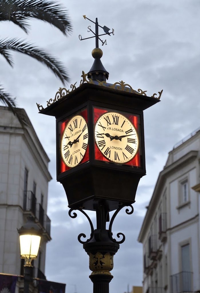Primer plano del histórico reloj de Losada en la Plaza del Arenal de Jerez de la Frontera, destacando su estructura de hierro forjado, las esferas iluminadas y la veleta superior.