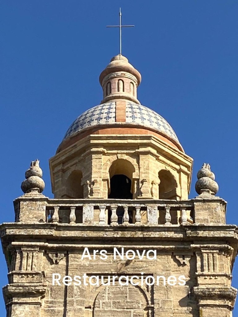 Plano medio del templete y la cúpula azulejada de la Torre de la Iglesia Mayor de Santa María la Coronada en Medina Sidonia tras las obras de rehabilitación, coronada por una cruz metálica sobre un cielo despejado.