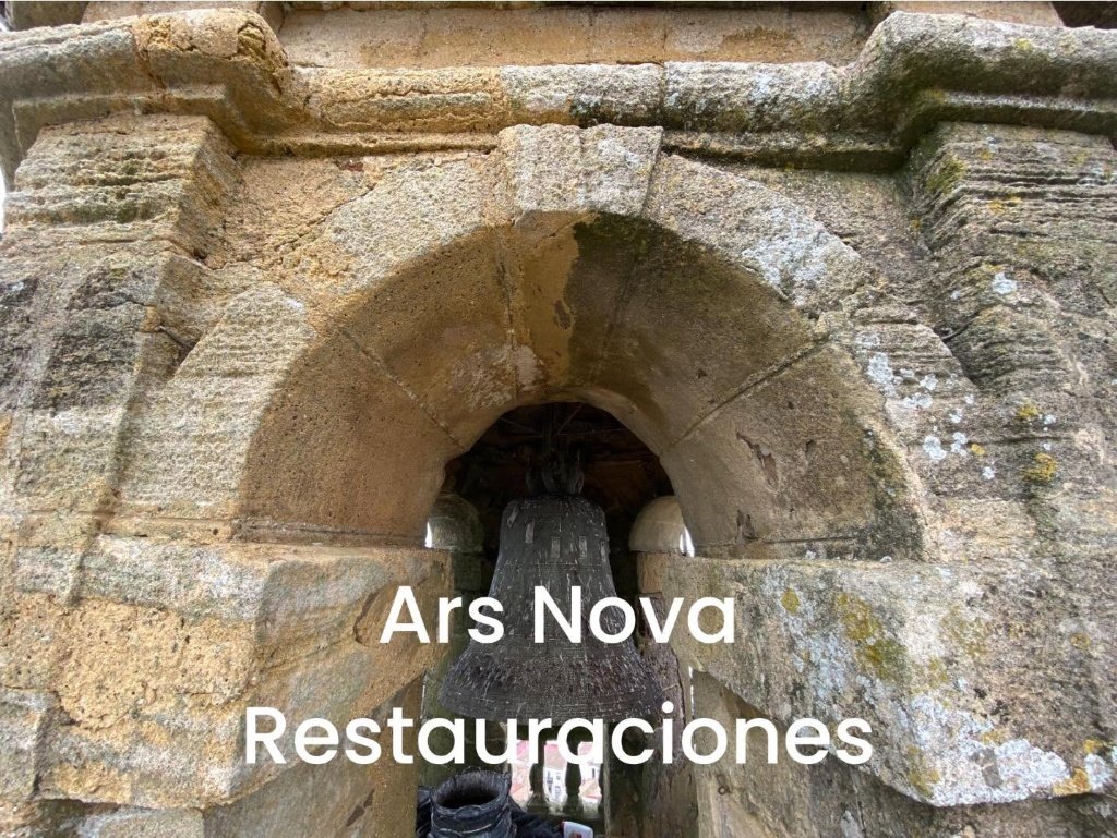 Primer plano de uno de los arcos de medio punto de la torre de Santa María la Coronada en Medina Sidonia, con una gran campana de bronce visible en el interior y la fábrica de piedra arenisca restaurada.