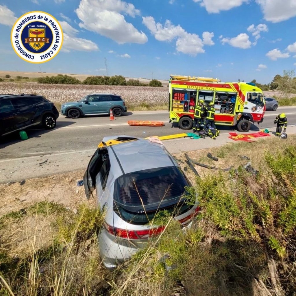 Vehículo plateado volcado en la cuneta de la carretera A-2078 durante las labores de rescate de los Bomberos en El Puerto de Santa María.