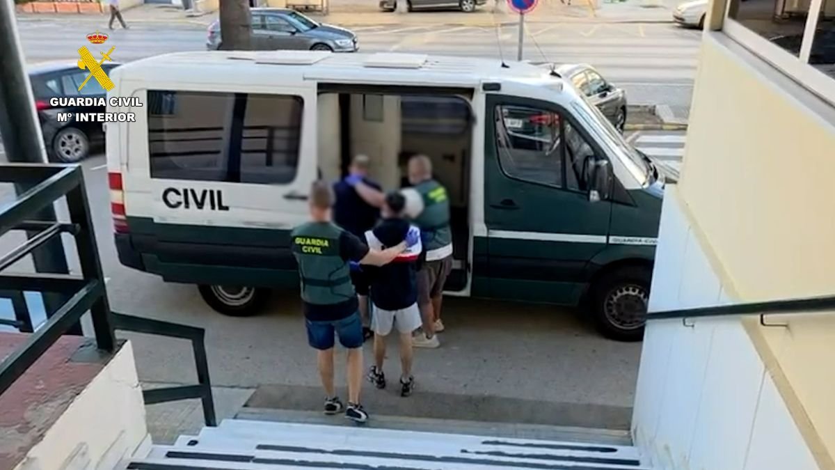 Agentes de la Guardia Civil custodian y trasladan a uno de los detenidos hacia el interior de un furgón oficial del cuerpo durante la operación en Conil de la Frontera.