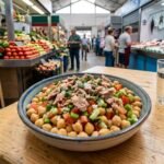 Ensalada templada de garbanzos de la Janda con piriñaca jerezana y atún de almadraba, servida en un plato hondo de cerámica sobre un fondo de madera clara con luz natural.